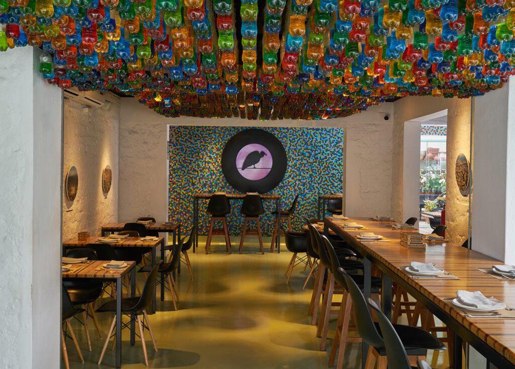 Cosme Dinner with bottle caps around the logo wall on the back and color bottles on top | Photo by Cosme