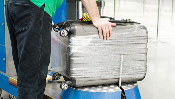 Worker wraps suitcase with a transparent film before travel by a